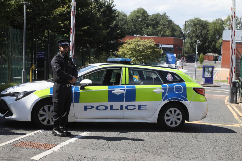 Police officer standing next to a police car at a crime scene.