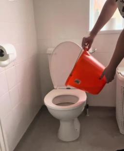 Person pouring water from an orange bucket into a toilet.