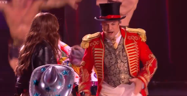 Screenshot of a ringmaster in a red coat and top hat interacting with a woman.