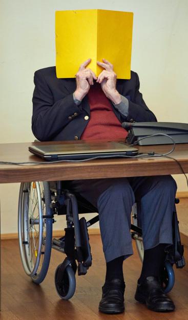 Former SS guard Bruno Dey in a wheelchair hides his face with a yellow folder during his trial.