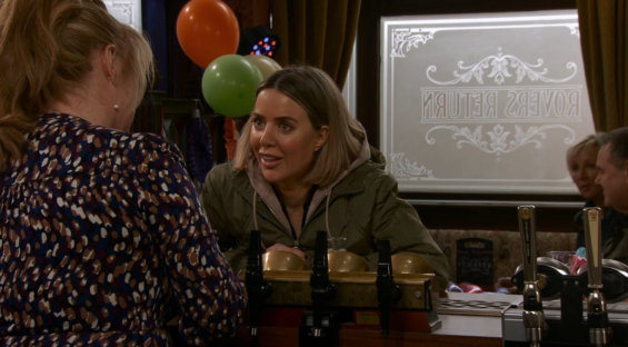 Screenshot of two women talking at a bar with balloons in the background.