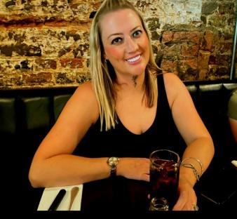 Woman sitting at a table with a drink, smiling.