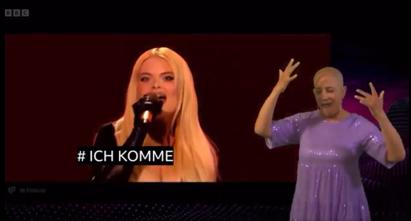Singer performing on stage with a sign language interpreter.