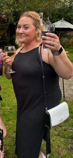 Woman in black dress holding two drinks.
