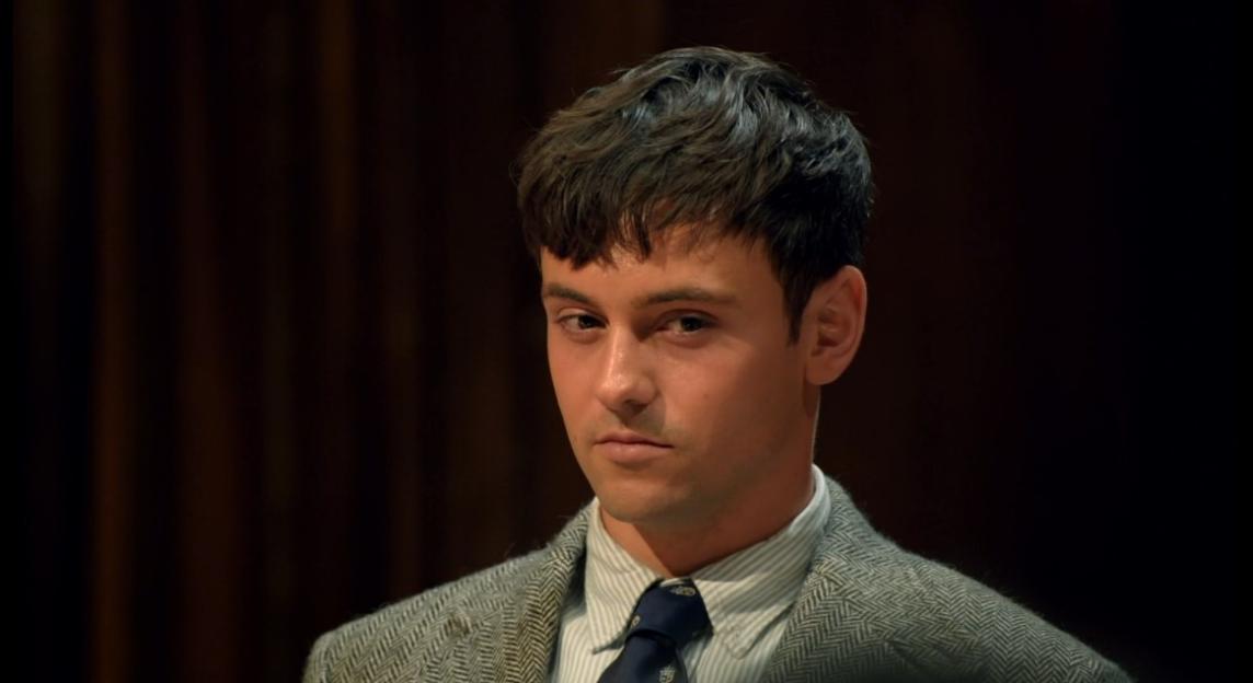 Young man in a gray tweed jacket and striped shirt with a dark blue tie.