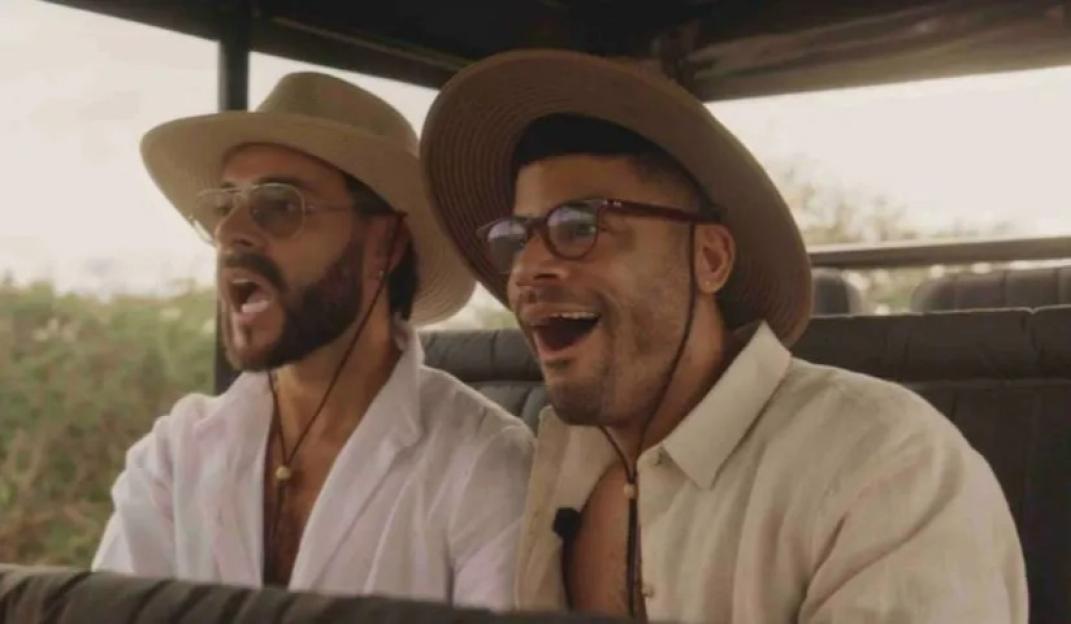 Two men wearing hats and glasses looking surprised while sitting in a vehicle.
