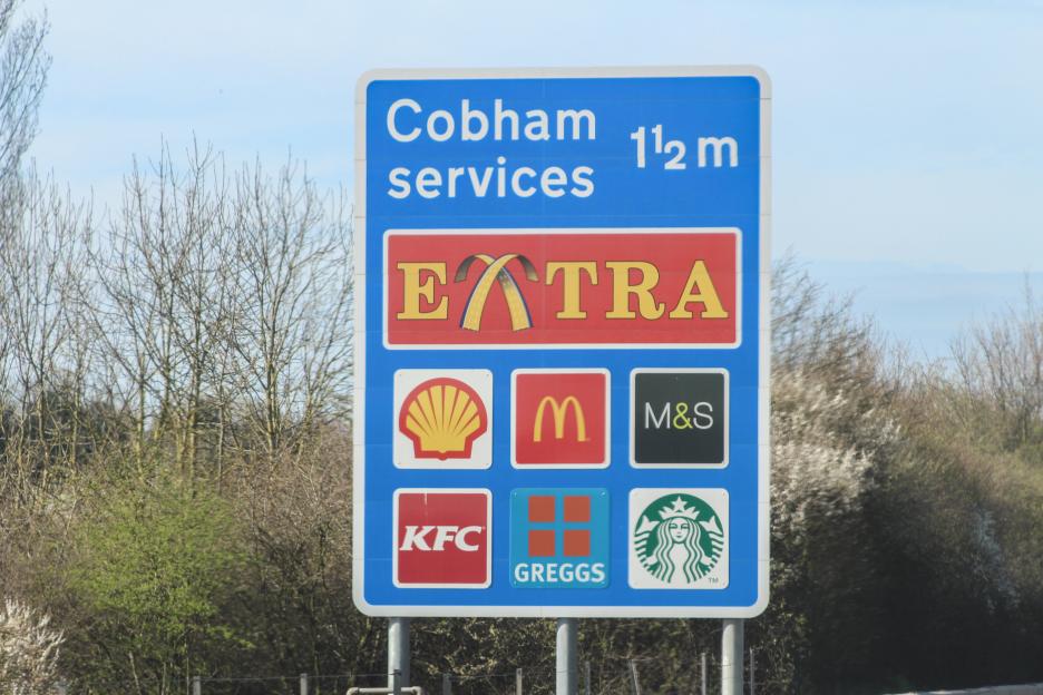 Blue motorway sign for Cobham services with logos for Shell, McDonald's, M&S, KFC, Greggs, and Starbucks.