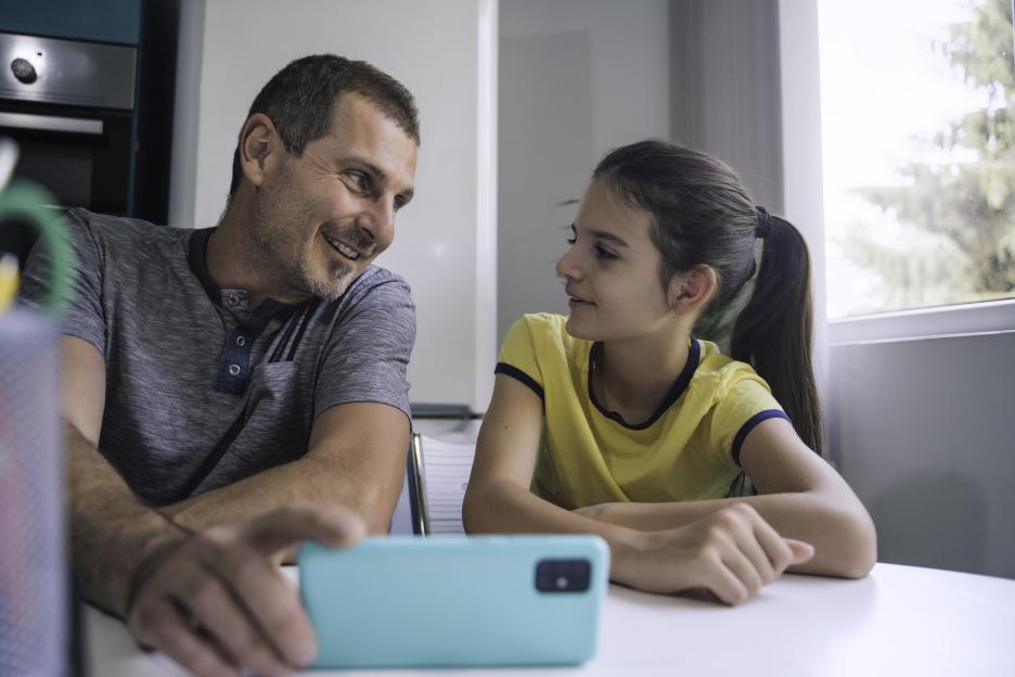 A father and daughter smiling while looking at a smartphone together.