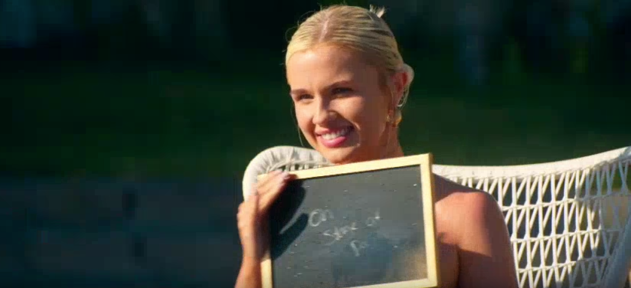 A blonde woman smiles while holding a small chalkboard that reads "On Store at P..."