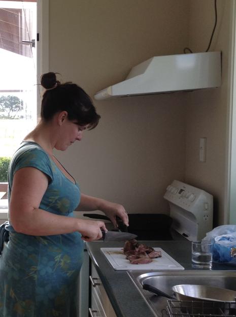 Woman cutting meat in a kitchen.