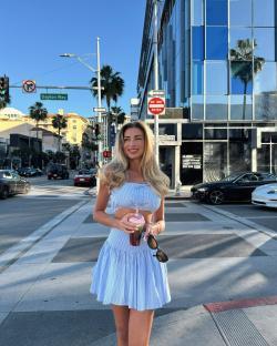 Woman in blue striped crop top and skirt holding a drink on a city street.