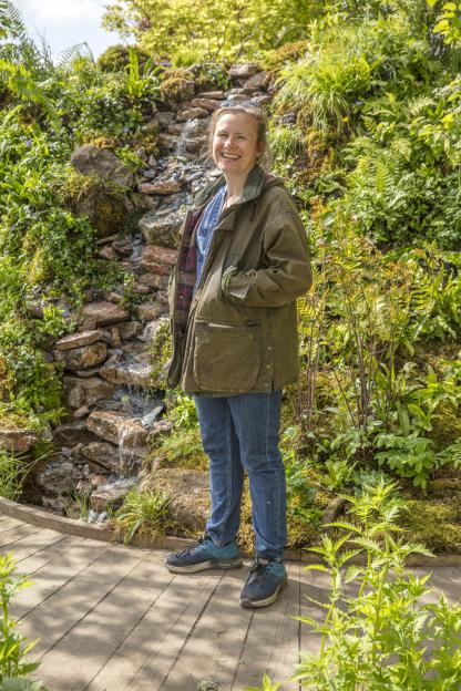 Woman smiling in front of a rock garden with a small waterfall.