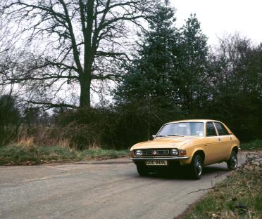 A tan Austin Allegro driving down a country road.