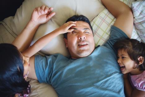 Two toddler girls waking their father up from a nap.