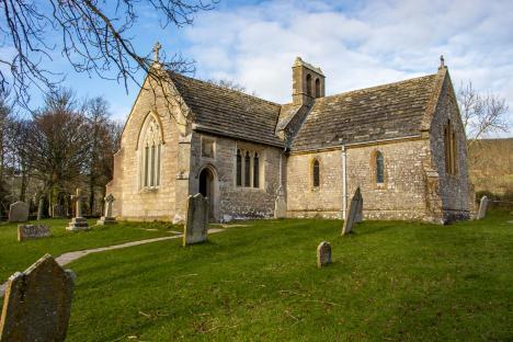 Stone church in Tyneham, Dorset, with surrounding graveyard.