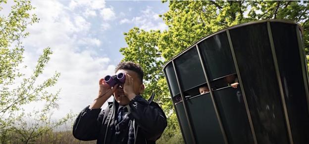 Boy using binoculars near a bird watching hide.