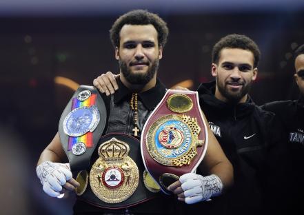 Moses Itauma celebrates a boxing victory, holding multiple championship belts.