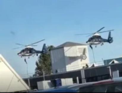 Two helicopters lowering people onto a building.