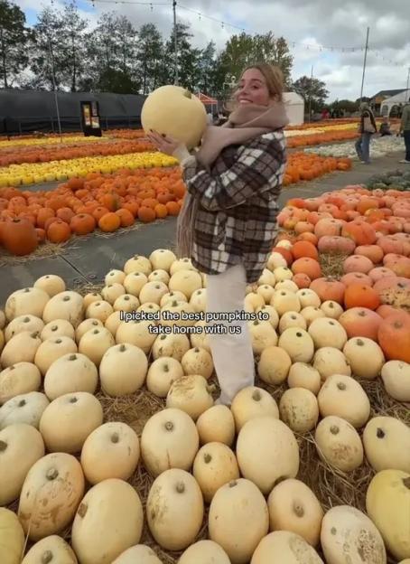 A woman holding a large white pumpkin in a pumpkin patch.