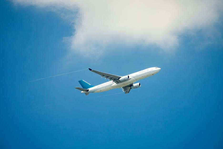 Illustration of a white passenger jet flying through a partly cloudy blue sky.