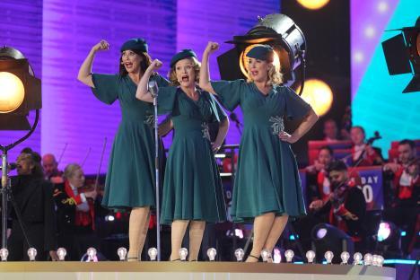 Three women in teal dresses singing at a VE Day concert.