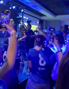 Screenshot of a celebratory gathering of people in blue jerseys.