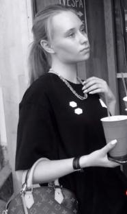Black and white photo of a young woman holding a Louis Vuitton handbag and a disposable cup.