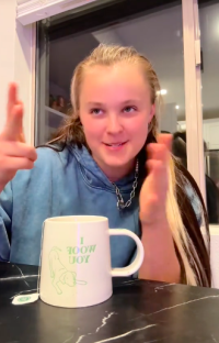 Person gesturing while sitting at a table with a mug that says