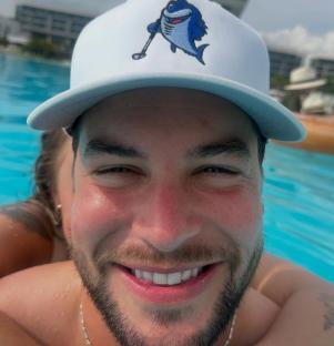 Close-up of a smiling man in a pool, wearing a white baseball cap.