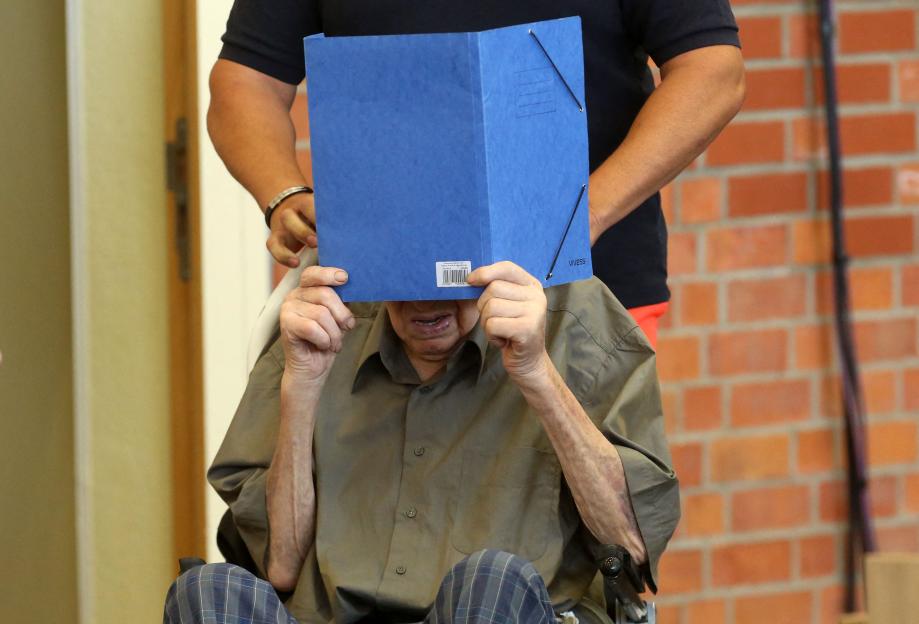 Josef Schuetz, a former Nazi concentration camp guard, hiding his face behind a blue folder.