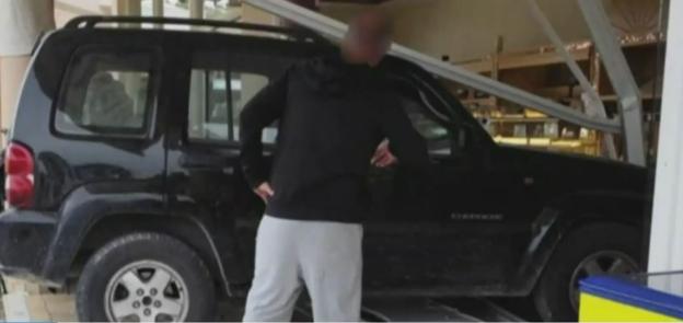 A person standing next to a black SUV with a damaged roof.