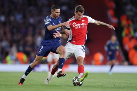Achraf Hakimi of Paris Saint-Germain and Jakub Kiwior of Arsenal competing for the ball during a soccer match.