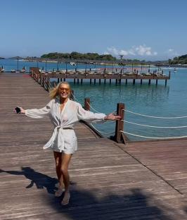 Tess Daly on a dock by the water, wearing a white shirt and sunglasses.