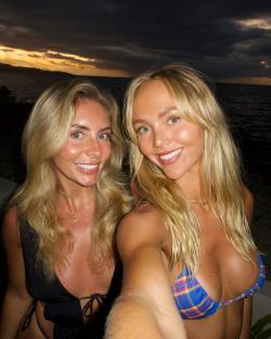Selfie of two blonde women in bikinis at sunset.