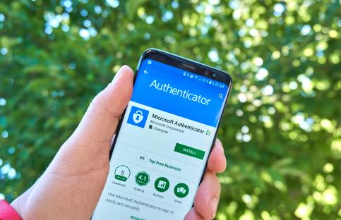 Hand holding a smartphone displaying the Microsoft Authenticator app.
