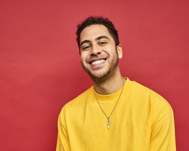 Portrait of a smiling young man wearing a yellow shirt and an ankh necklace.