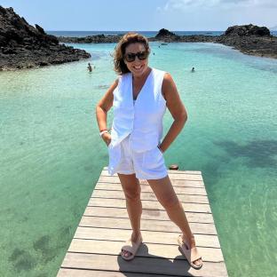 Jane McDonald on a dock by clear water.