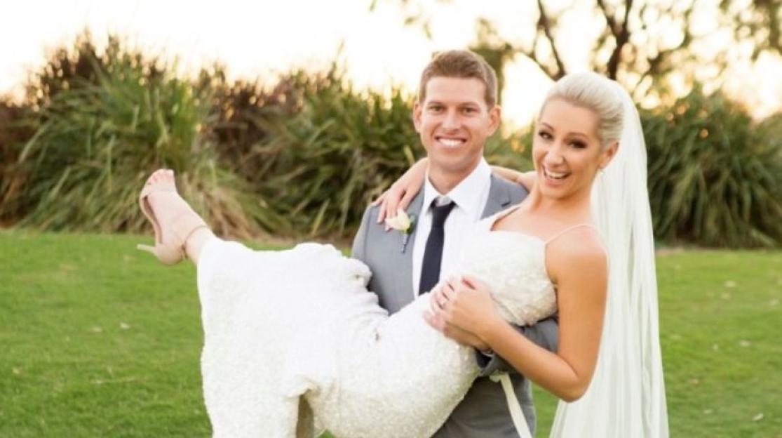 Matt Conwell carrying Ashleigh L. Conwell in her wedding dress, both smiling at the camera.