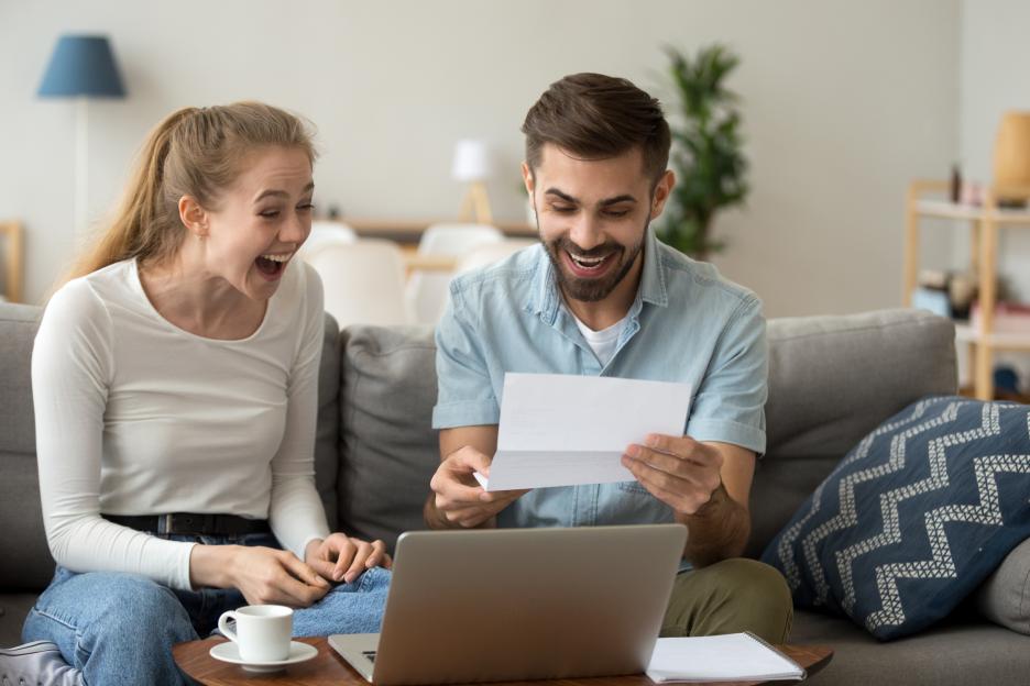 Happy couple excitedly reading good news together on their couch.