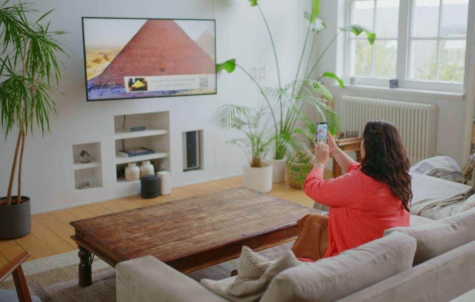 Woman taking a photo of a pyramid on a TV screen with her phone.