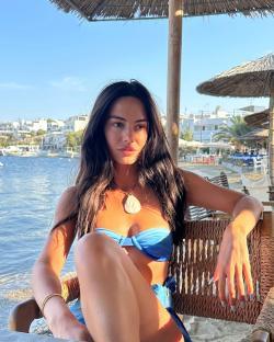 Woman in blue bikini sitting at a seaside cafe.