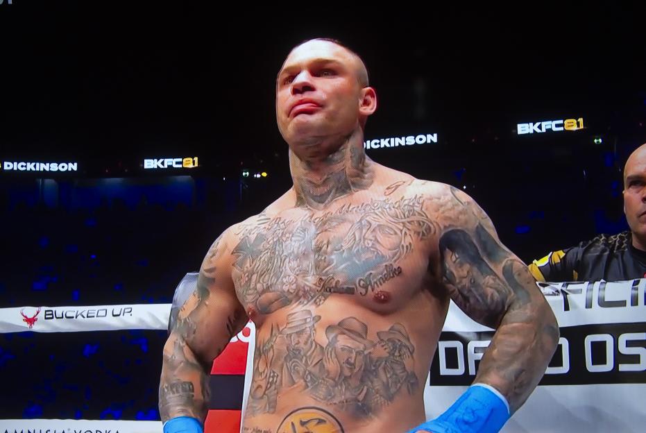 David Oscar, a bare-knuckle fighter, looking up with a serious expression, covered in tattoos on his chest, shoulders, and arms.
