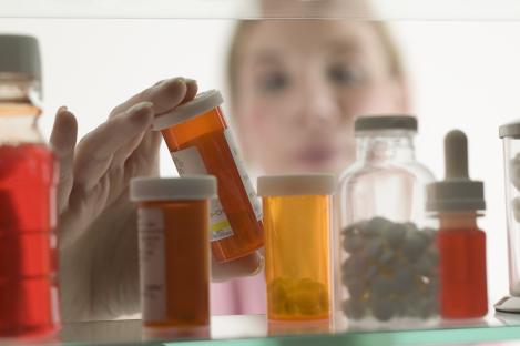 Woman's hand taking prescription medication from a medicine cabinet.