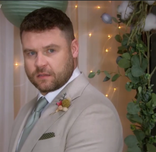 Screenshot of a man in a light beige suit.