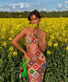 Woman in colorful crochet dress in a field of yellow flowers.