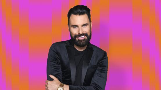 Rylan, smiling, in a black velvet jacket.
