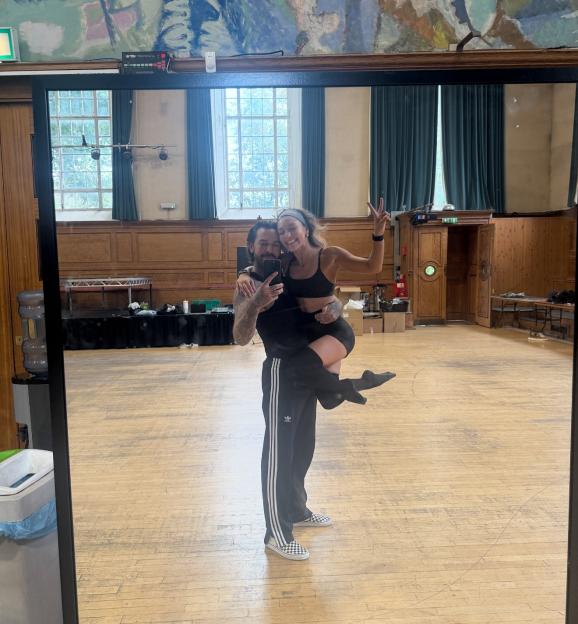 Mirror selfie of a man holding a woman in a dance studio.