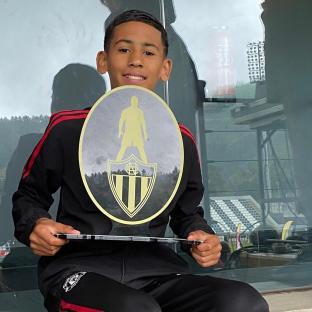 Boy holding an award with a soccer player silhouette and team logo.