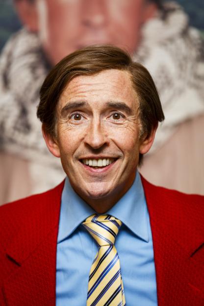 Steve Coogan as Alan Partridge with a wide smile, wearing a blue shirt, red blazer, and yellow striped tie.