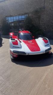 Red and white Porsche race car parked in front of a stone building.
